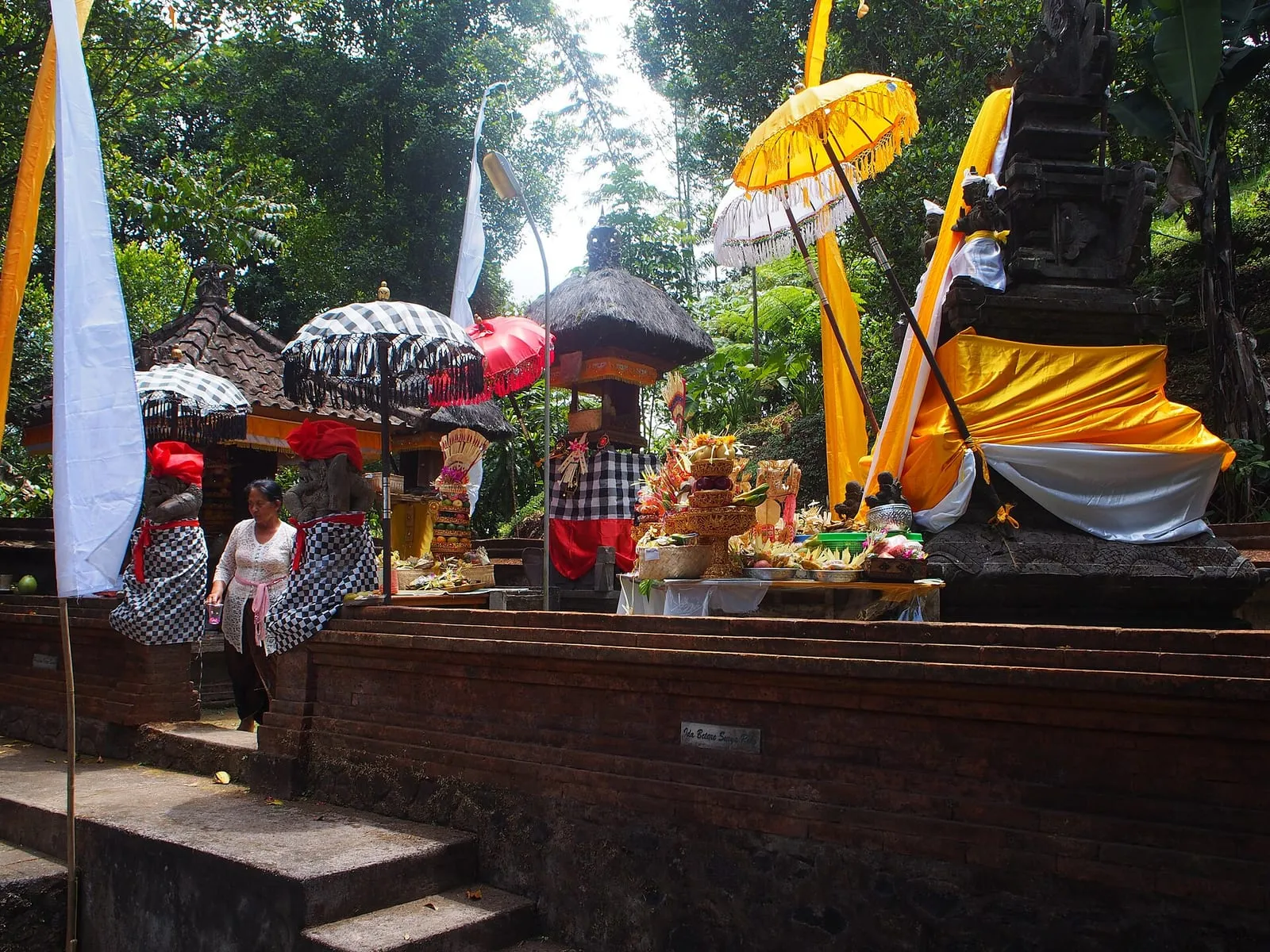 A decorated Balinese temple shrine with ceremonial umbrellas and food offerings during a temple ceremony